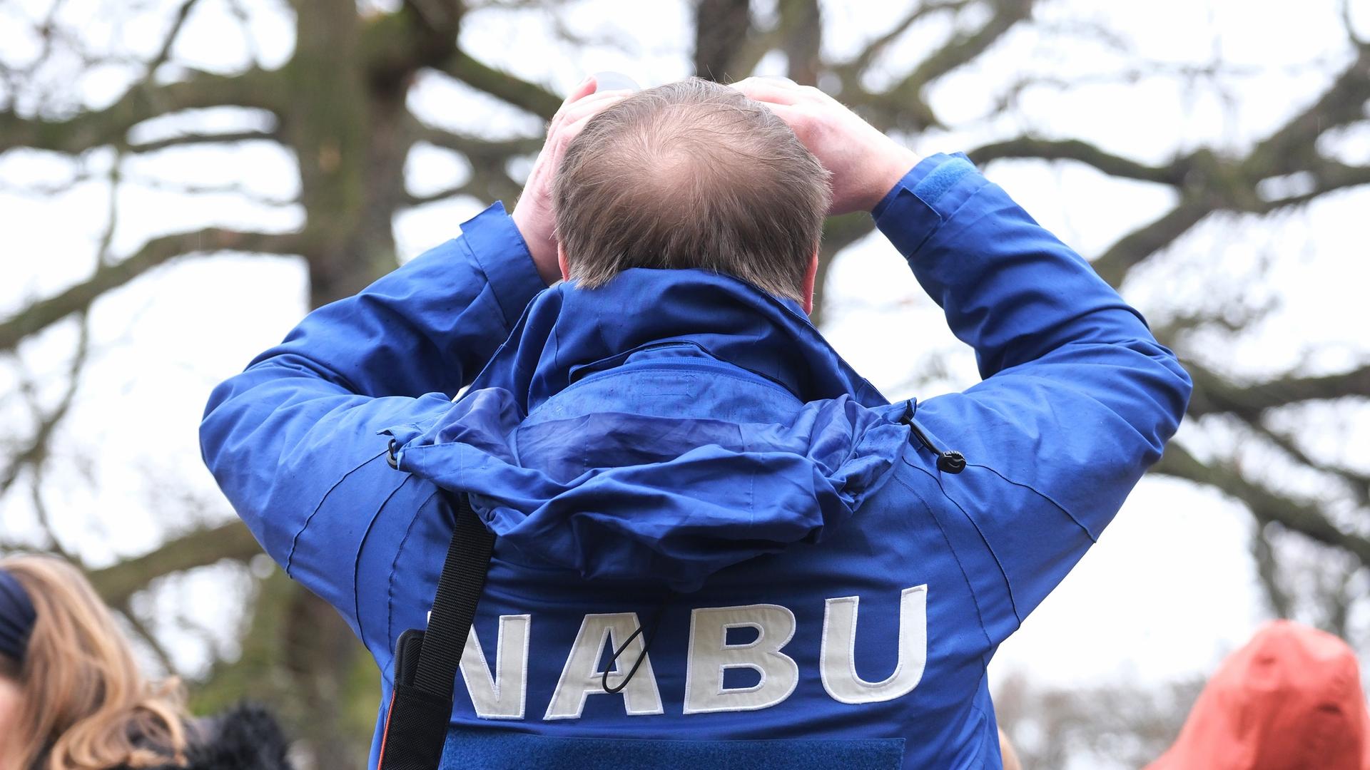 Das Foto zeigt einen Mann mit blauer Jacke und der Aufschrift Nabu. Er steht mit dem Rückem zum Betrachter und blickt durch ein Fernglas, um Vögel zu beobachten.