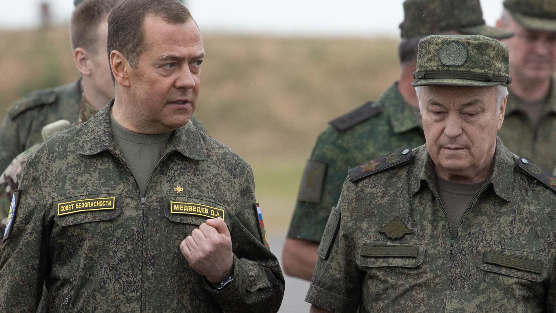 Dmitri Medwedew trägt Tarnfarben und spricht mit Militärbeamten. Dabei ballt er seine linke Hand zur Faust.