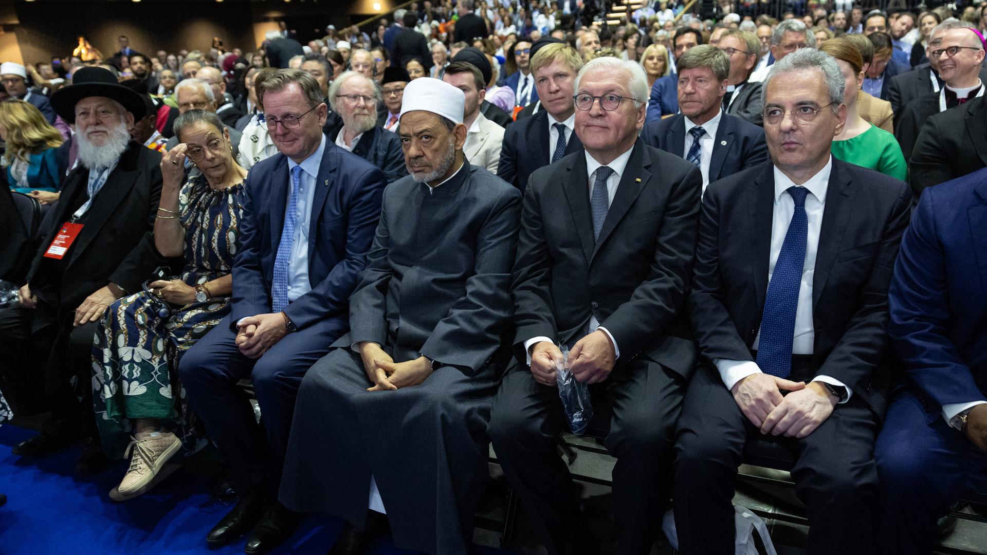 Marco Impagliazzo (r-l), Präsident von Sant Â·Egidio, Bundespräsident Frank-Walter Steinmeier, Großimam Ahmed Mohammed Ahmed al-Tayyeb, Bodo Ramelow (Die Linke), Ministerpräsident von Thüringen, seine Ehefrau Germana Alberti vom Hofe und der Berliner Rabbiner Chaim Yitshak Ehrenberg sitzen in der ersten Reihe in der Venti-Music Hall. Hinter ihnen sitzen viele weitere Zuschauer.