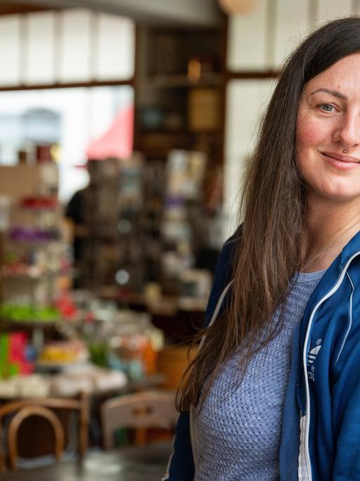 Nina Fuchs steht im Türrahmen eines Geschäfts und lächelt, sie trägt eine blaue Adidas-Jacke.