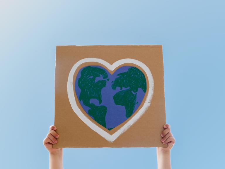 Ein junger Umweltschützer hält ein Schild in die Luft. Darauf ist ein Globus in Herzform.
