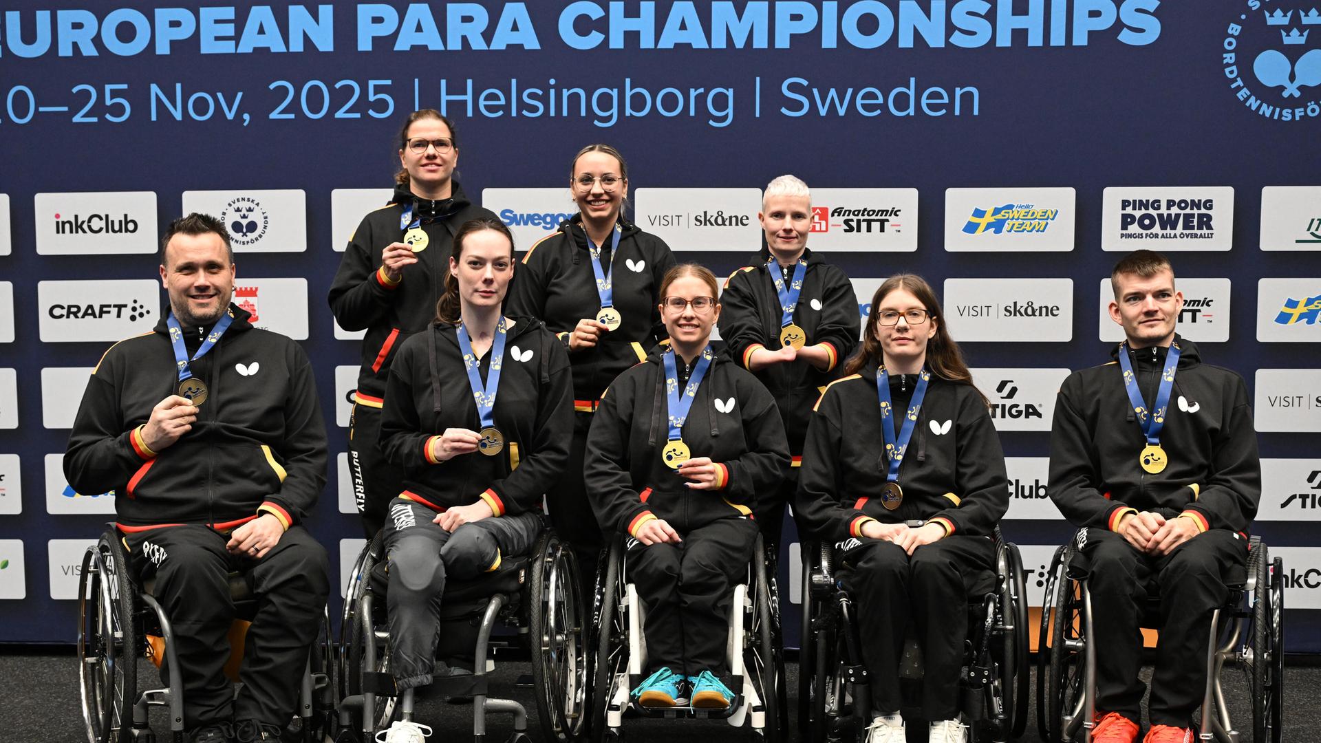 Die Medaillen-Gewinner sitzen und stehen und zeigen ihre Medaillen. 