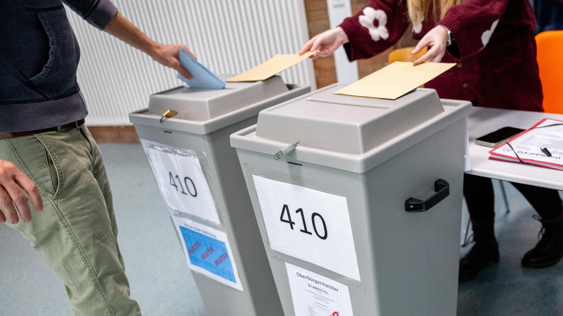 Ein Wähler wirft in einem Wahllokal, das im Foyer einer Grundschule untergebracht ist, seinen Stimmzettel für die Kommunalwahl in eine Wahlurne. 