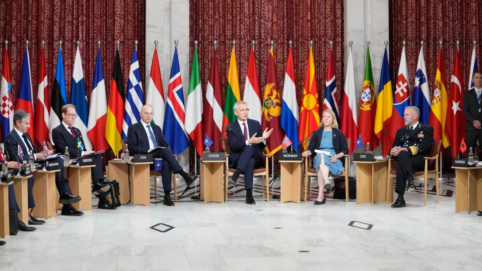 NATO-Generalsekretär Stoltenberg spricht mit den Außenministern der Mitgliedsstaaten. Hinter ihnen die Landesfahnen.