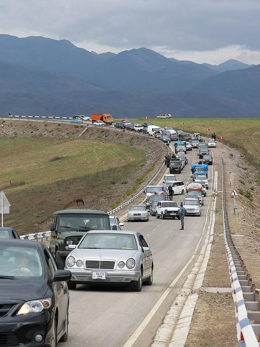 Flüchtende aus Bergkarabach warten in Autos in einer Schlange auf einer Straße auf die Einreise nach Armenien. Im Hintergrund sind Berge des Kaukaus zu sehen. 