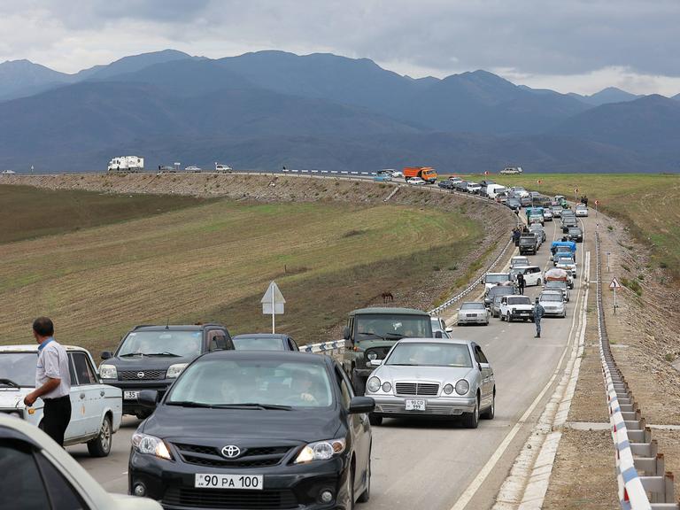 Flüchtende aus Bergkarabach warten in Autos in einer Schlange auf einer Straße auf die Einreise nach Armenien. Im Hintergrund sind Berge des Kaukaus zu sehen. 