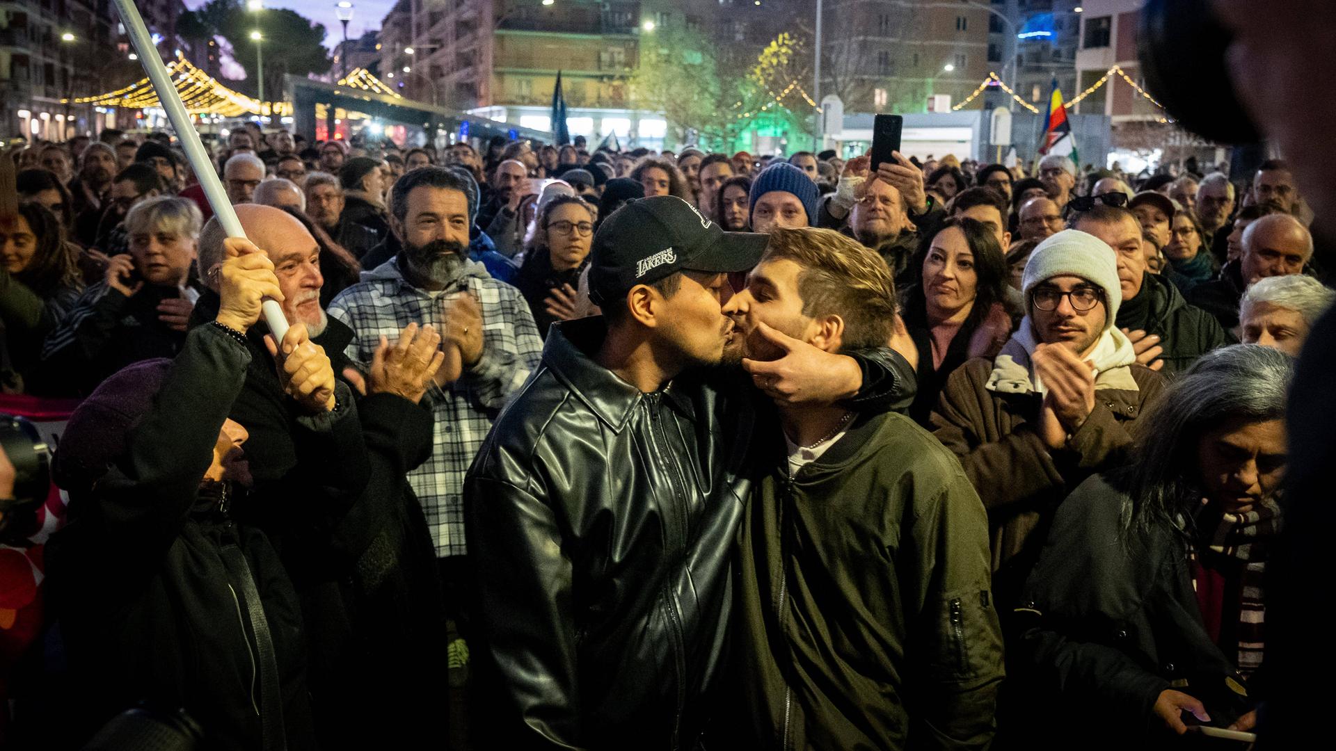 Zwei junge Männer küssen sich bei einer Demonstration gegen Homophobie in Rimini. Im Hintergrund applaudieren mehrere Menschen. Zwei junge Männer küssen sich bei einer Demonstration gegen Homophobie in Rimini. Im Hintergrund applaudieren mehrere Menschen.