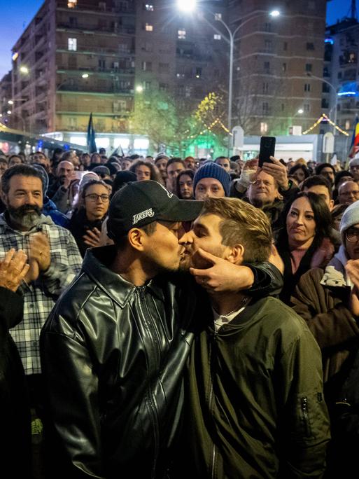 Zwei junge Männer küssen sich bei einer Demonstration gegen Homophobie in Rimini. Im Hintergrund applaudieren mehrere Menschen. 