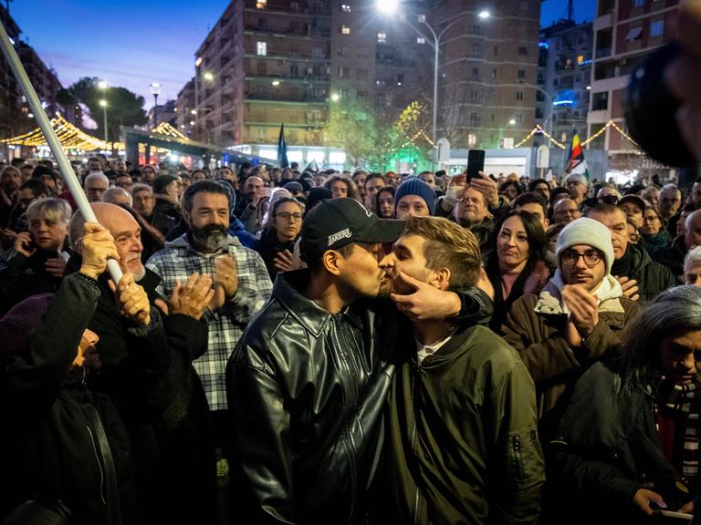 Zwei junge Männer küssen sich bei einer Demonstration gegen Homophobie in Rimini. Im Hintergrund applaudieren mehrere Menschen. 