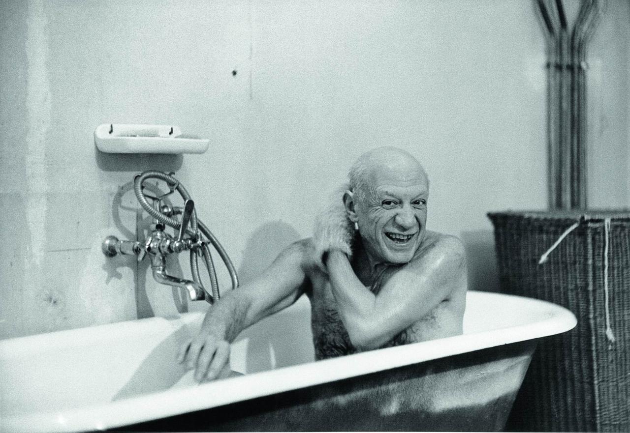 Der Künstler Pablo Picasso sitzt in einer Badewanne und lacht in die Kamera.
