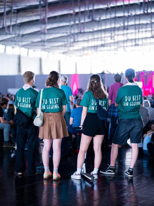 Junge Menschen stehen in einer Halle beim 39. Evangelischen Kirchentag mit T-Shirts mit dem Slogan "Du bist ein Gewinn. 