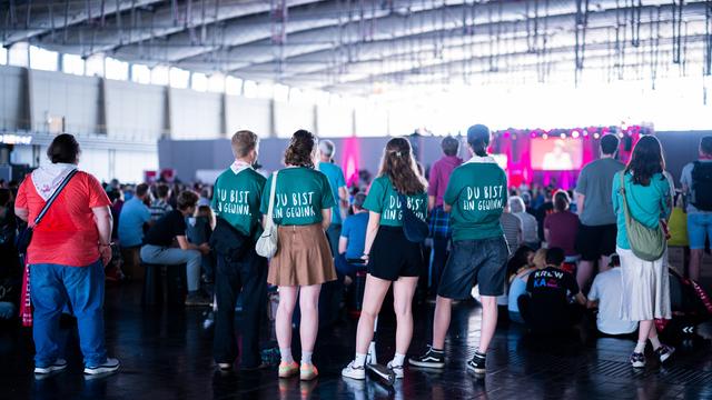 Junge Menschen stehen in einer Halle beim 39. Evangelischen Kirchentag mit T-Shirts mit dem Slogan "Du bist ein Gewinn. 