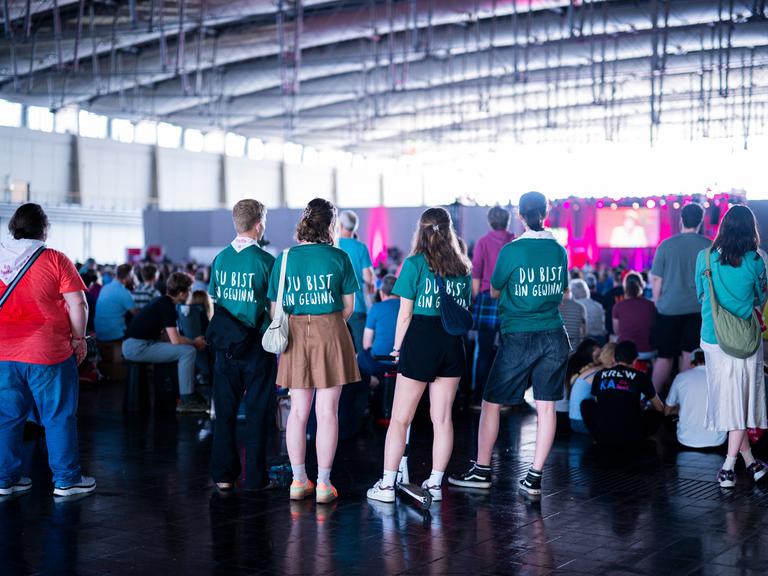 Junge Menschen stehen in einer Halle beim 39. Evangelischen Kirchentag mit T-Shirts mit dem Slogan "Du bist ein Gewinn. 