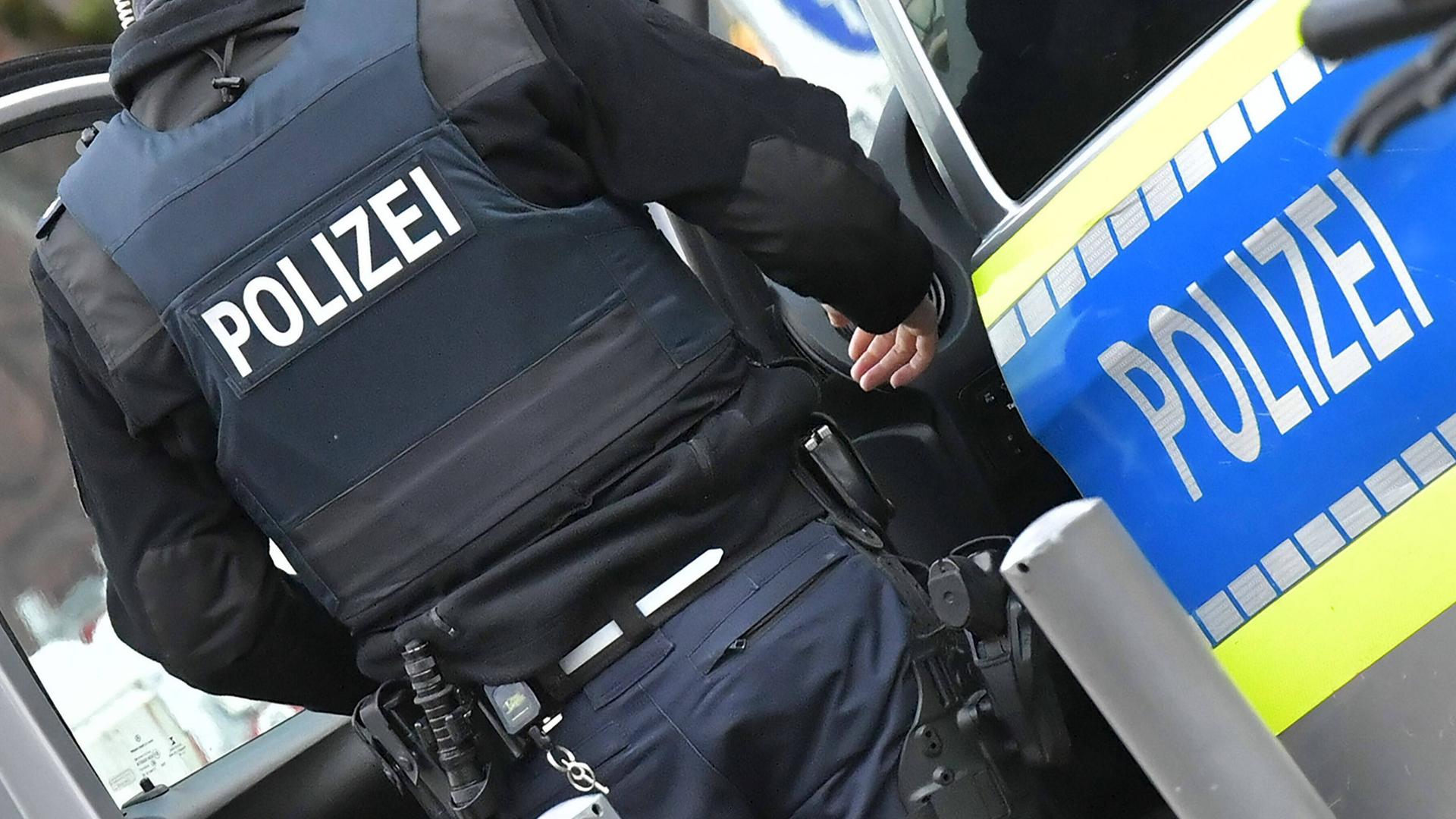 Ein Polizist steht vor einem Polizeiauto, man sieht ihn von hinten.