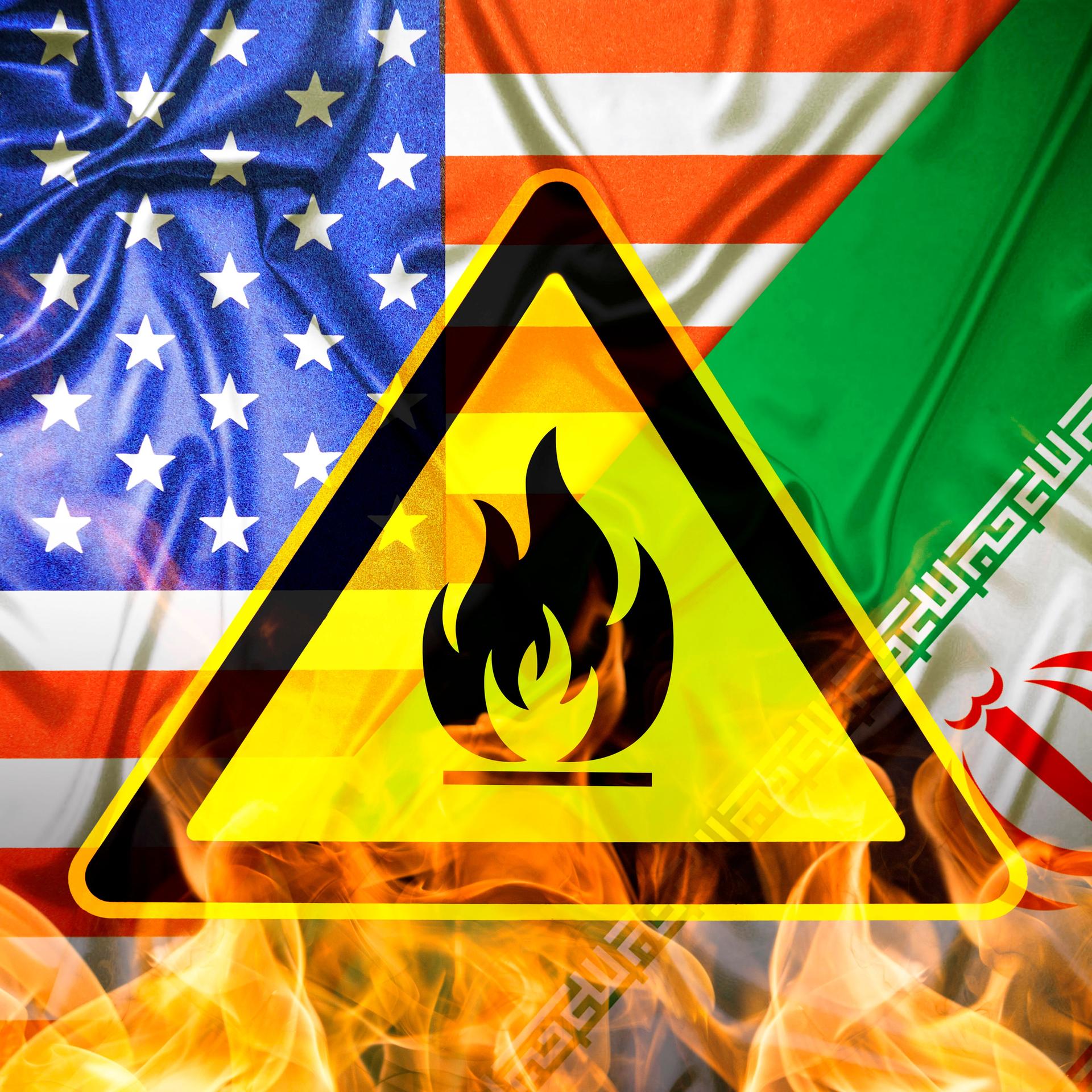 Das Bild zeigt eine Kombo aus den Flaggen der USA und des Iran, unter denen Flammen zu sehen sind. Davor montiert ist ein gelb-schwarzes Gefährdungszeichen.