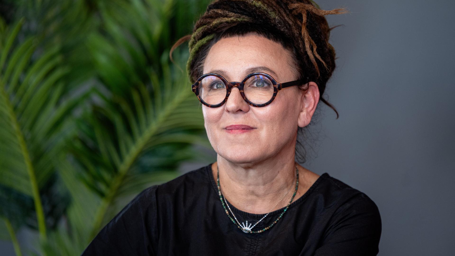 Olga Tokarczuk trägt eine runde, schwarz umrandete Brille und ein schwarzes Oberteil. Sie schaut zur Seite und lächelt. Olga Tokarczuk trägt eine runde, schwarz umrandete Brille und ein schwarzes Oberteil. Sie schaut zur Seite und lächelt.