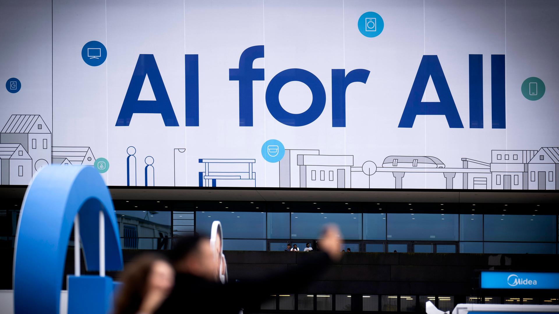 An einem Samsung Stand auf der IFA Berlin im Jahr 2024 steht in großen Buchstaben "KI for all" geschrieben. Davor sind in der Unschärfe einige Messebesucher zu sehen.