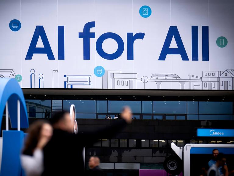 An einem Samsung Stand auf der IFA Berlin im Jahr 2024 steht in großen Buchstaben "KI for all" geschrieben. Davor sind in der Unschärfe einige Messebesucher zu sehen.