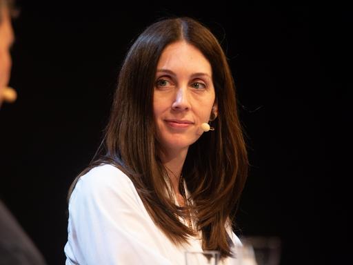 Eine Frau sitzt auf einer Bühne und blickt nach links. Es ist die US-Autorin Liz Moore. Sie hat braune lange Haare und trägt eine weiße Bluse. 