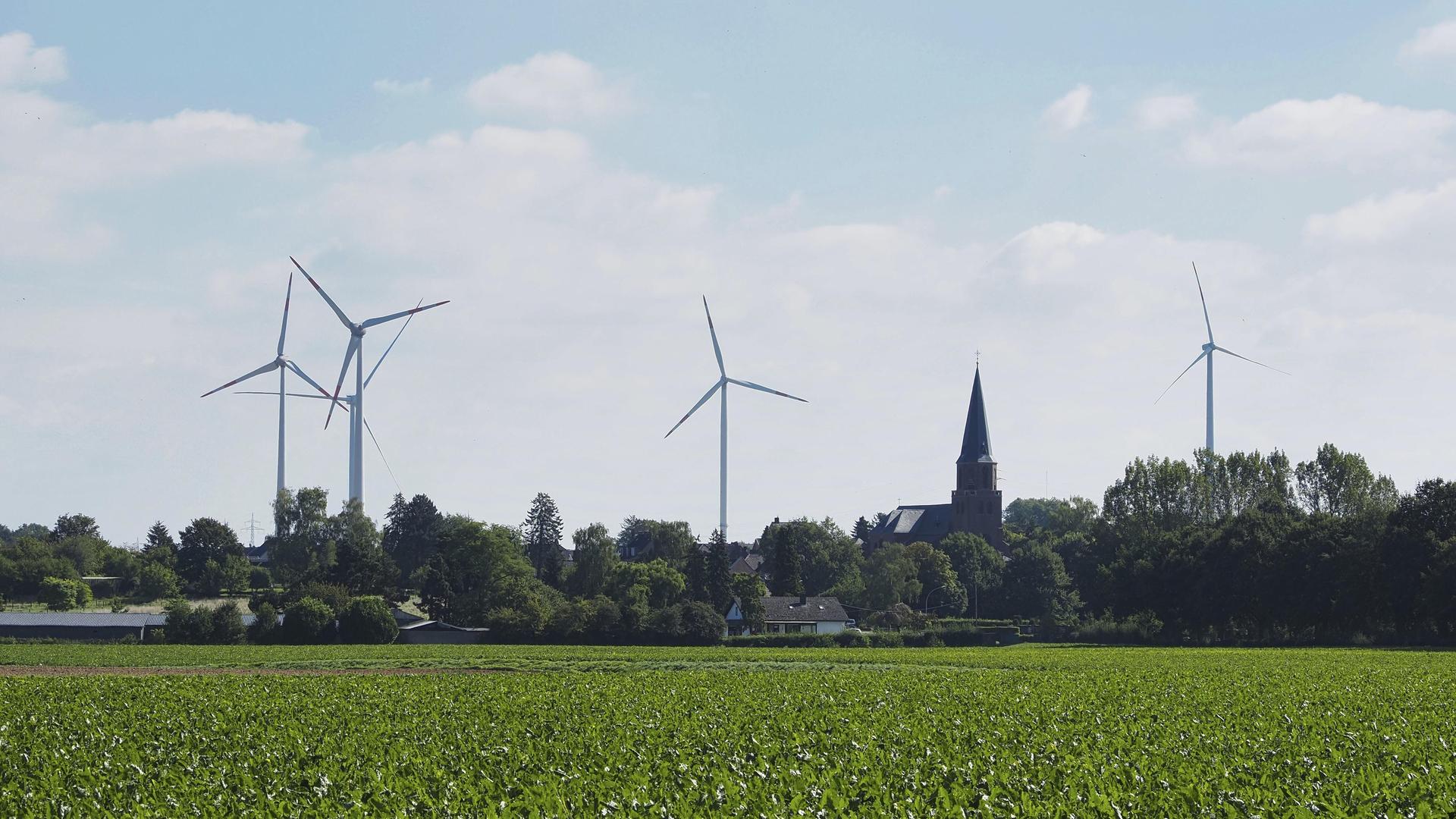 Windräder zur Stromerzeugung am Rande des Braunkohle Tagebau Garzweiler in NRW, dahinter ein Kirchturm.