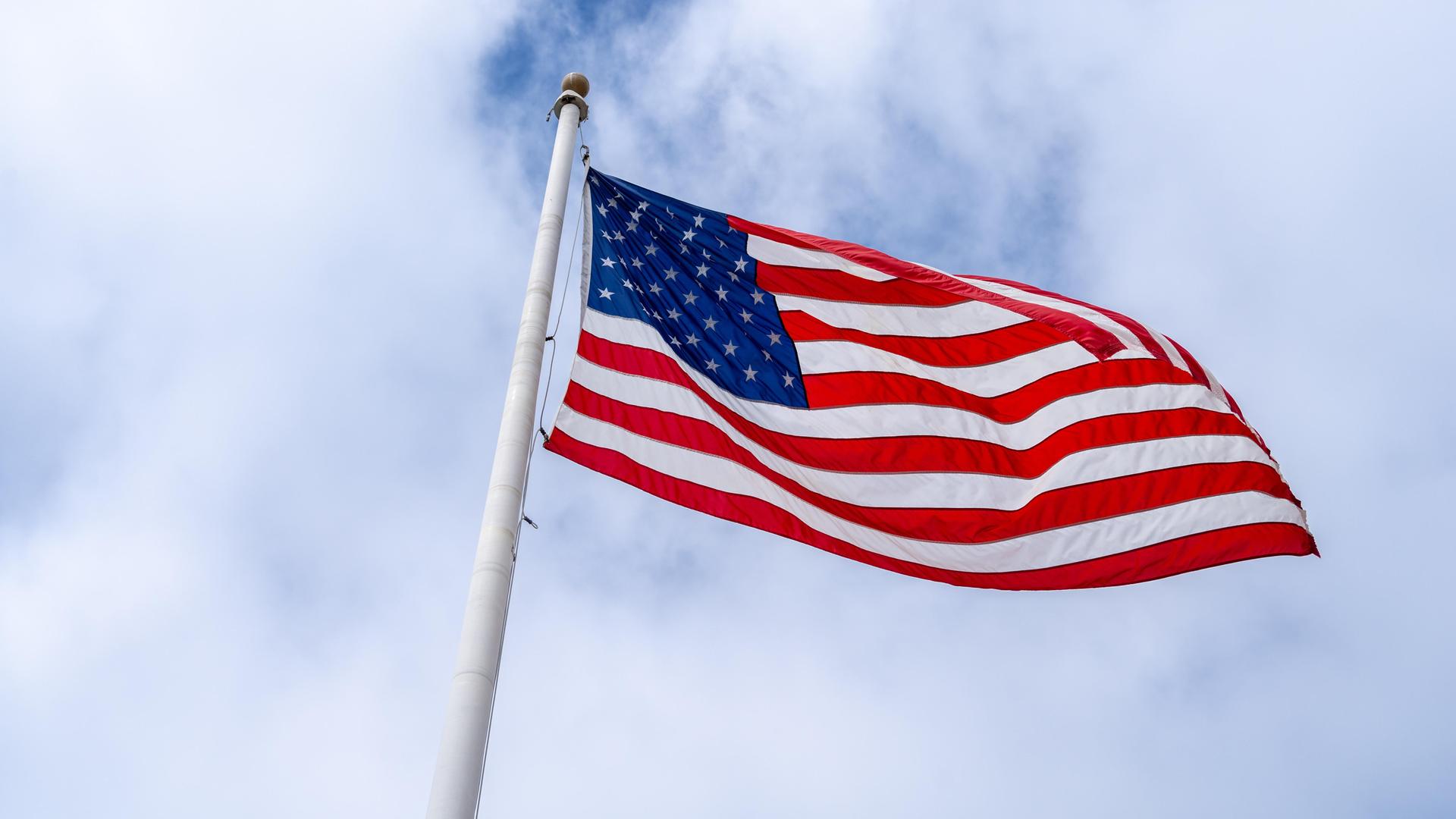 Eine amerikanische Flagge weht an einem hohen Mast vor einem bewölkten Himmel 