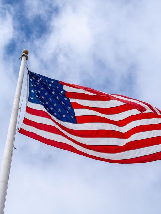 Eine amerikanische Flagge weht an einem hohen Mast vor einem bewölkten Himmel 