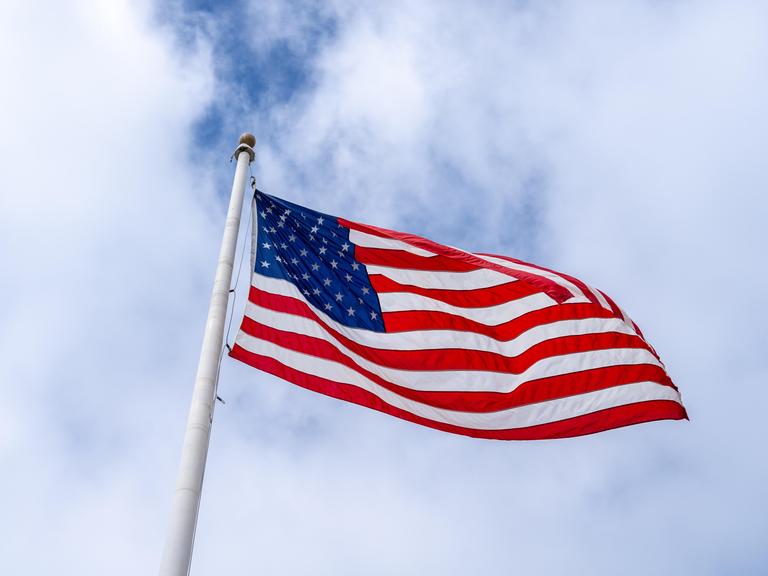 Eine amerikanische Flagge weht an einem hohen Mast vor einem bewölkten Himmel 