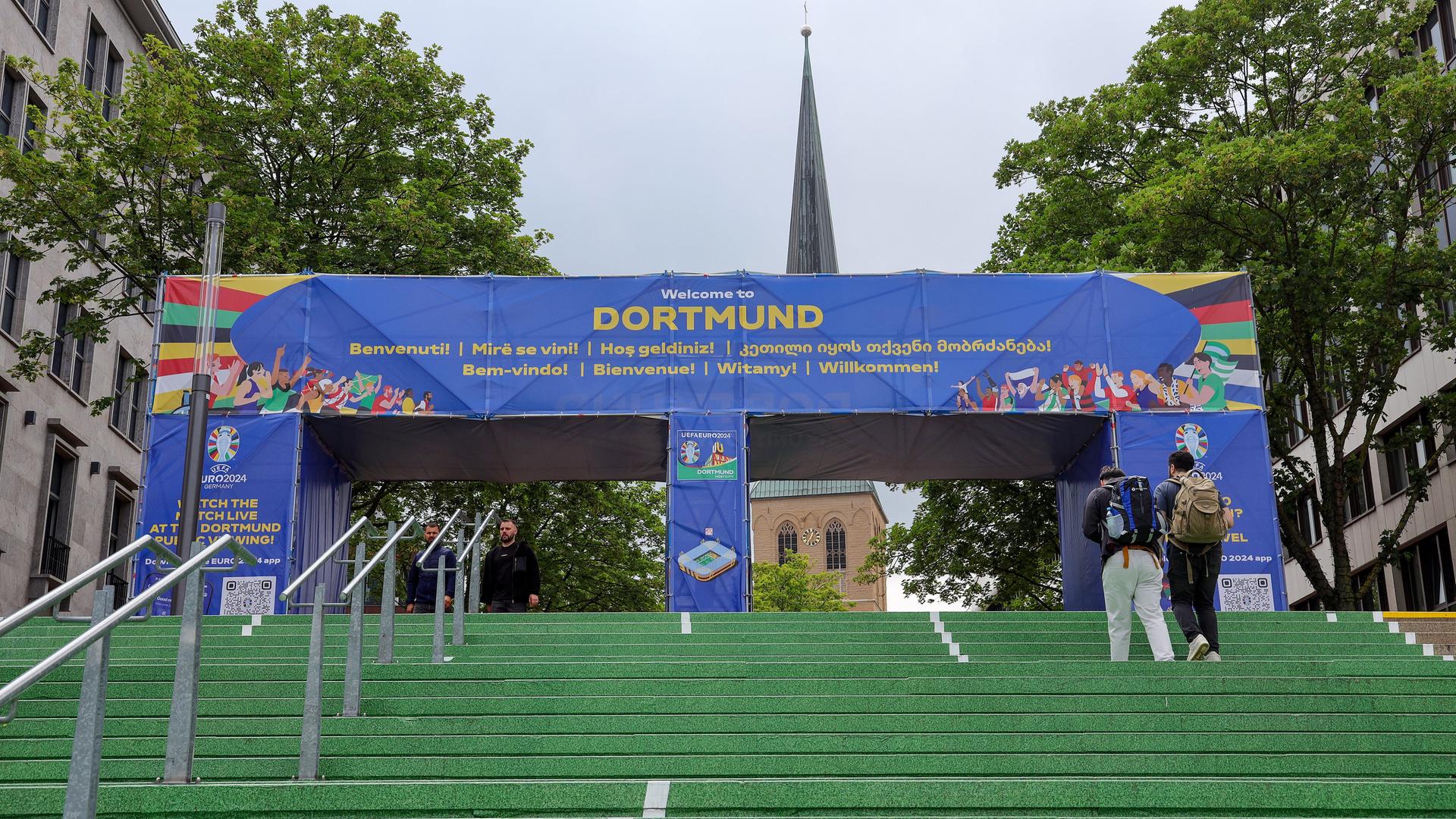 In der Nähe des Dortmunder Hauptbahnhofs führt ein grüner Teppich in Richtung Innenstadt. Darüber steht auf einem Bogen in den Farben der Euro "Dortmund" und "Willlkommen" in verschiedenden Sprachen.