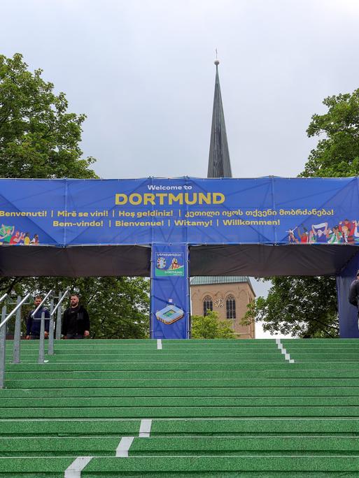 In der Nähe des Dortmunder Hauptbahnhofs führt ein grüner Teppich in Richtung Innenstadt. Darüber steht auf einem Bogen in den Farben der Euro "Dortmund" und "Willlkommen" in verschiedenden Sprachen.