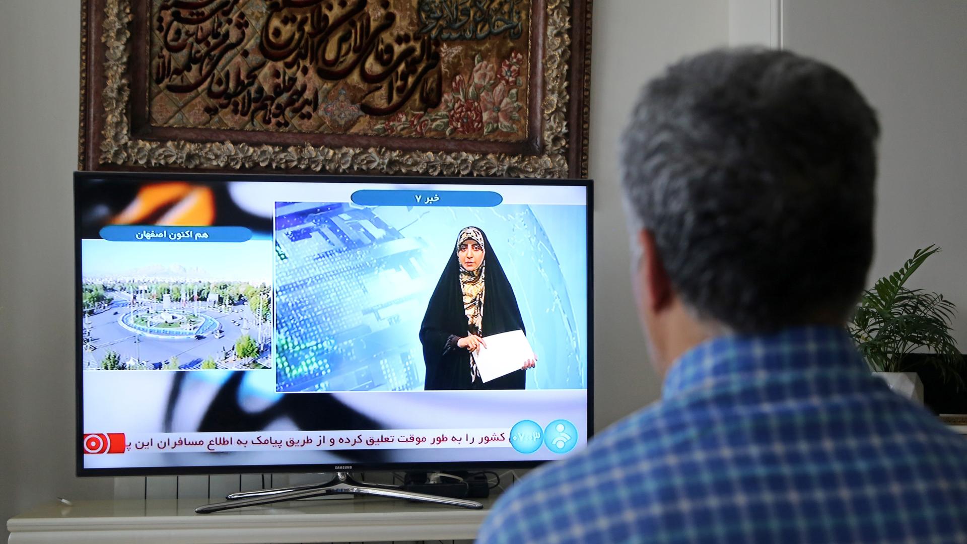 Ein Mann schaut einer Fernsehreporterin in Teheran zu, nachdem das offizielle iranische Fernsehen „massive Explosionen“ in der zentralen Provinz Isfahan bestätigt hat. 