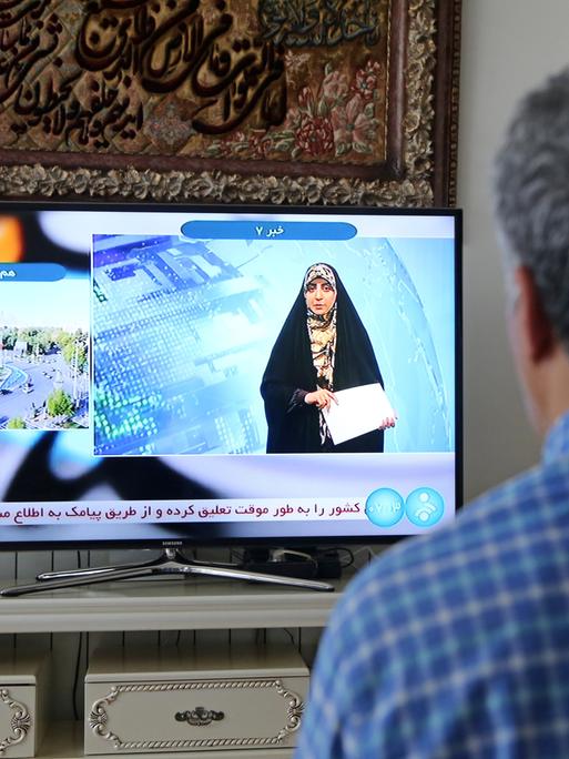 Ein Mann schaut einer Fernsehreporterin in Teheran zu, nachdem das offizielle iranische Fernsehen „massive Explosionen“ in der zentralen Provinz Isfahan bestätigt hat. 