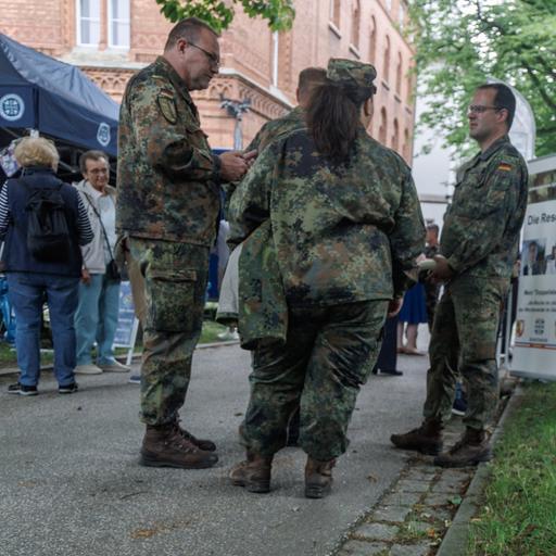 Informationsstände auf dem Veteranentag in Kiel. Bundeswehrsoldaten stehen in einer Gruppe. Daneben ist ein Plakat aufgestellt mit der Aufschrift: Die stärkste Friedensbewegung Deutschlands. 