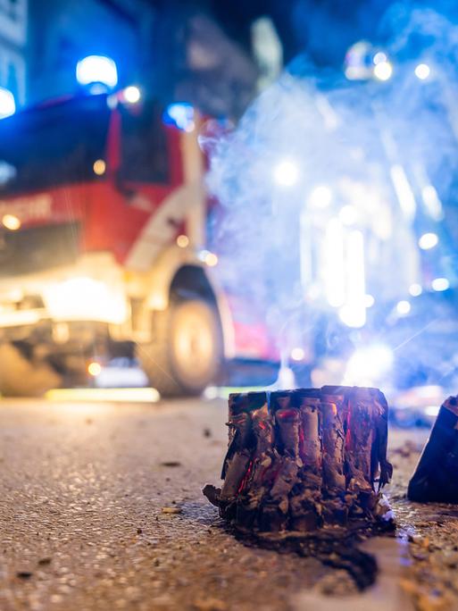 Abgebrannte Böller liegen auf einer Straße in Berlin, im Hintergrund steht ein Feuerwehrauto.