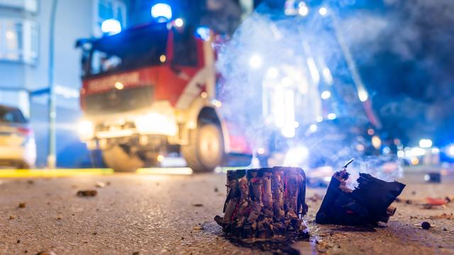 Abgebrannte Böller liegen auf einer Straße in Berlin, im Hintergrund steht ein Feuerwehrauto.