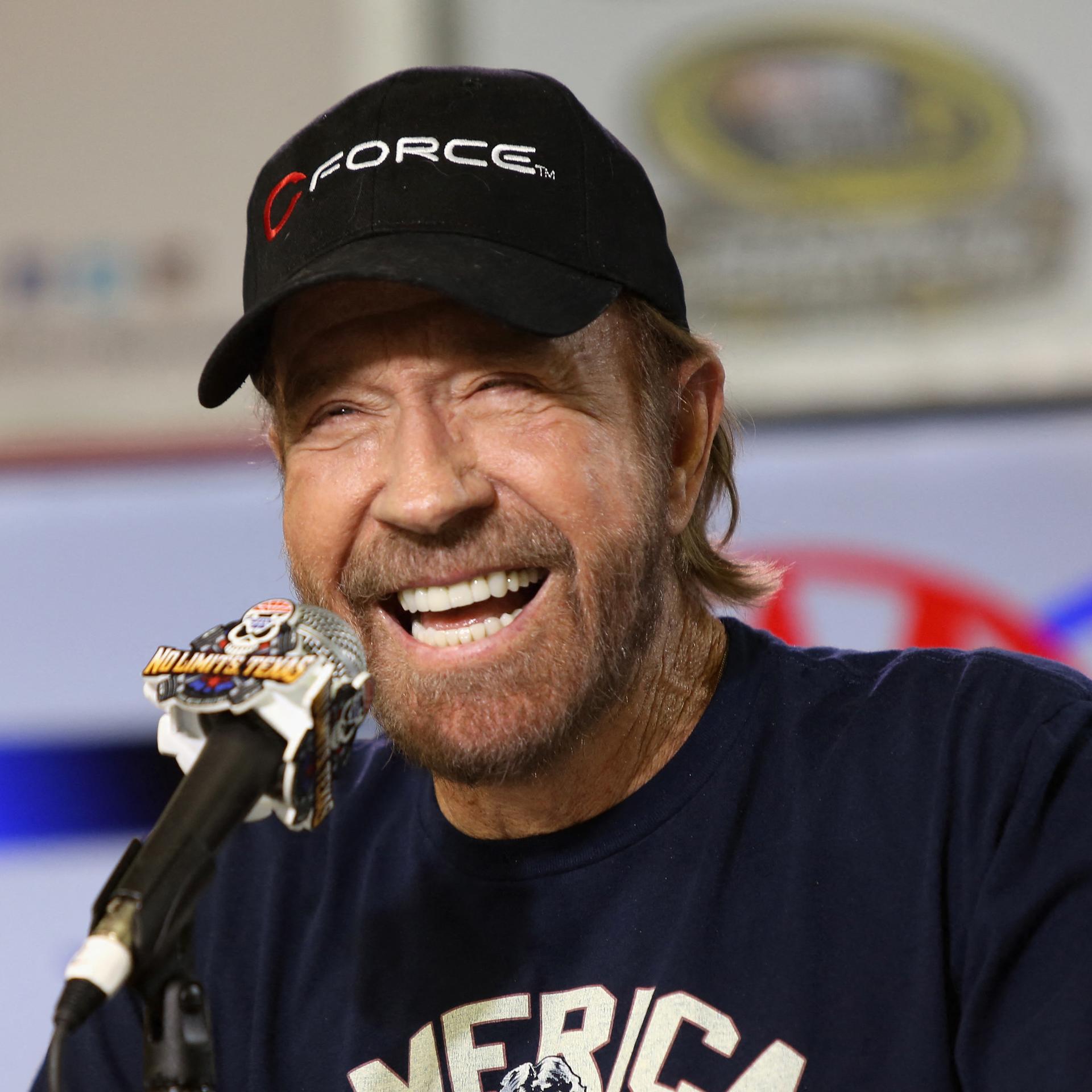 Der Schauspieler Chuck Norris sitzt vor einem Mikrofon und lacht.