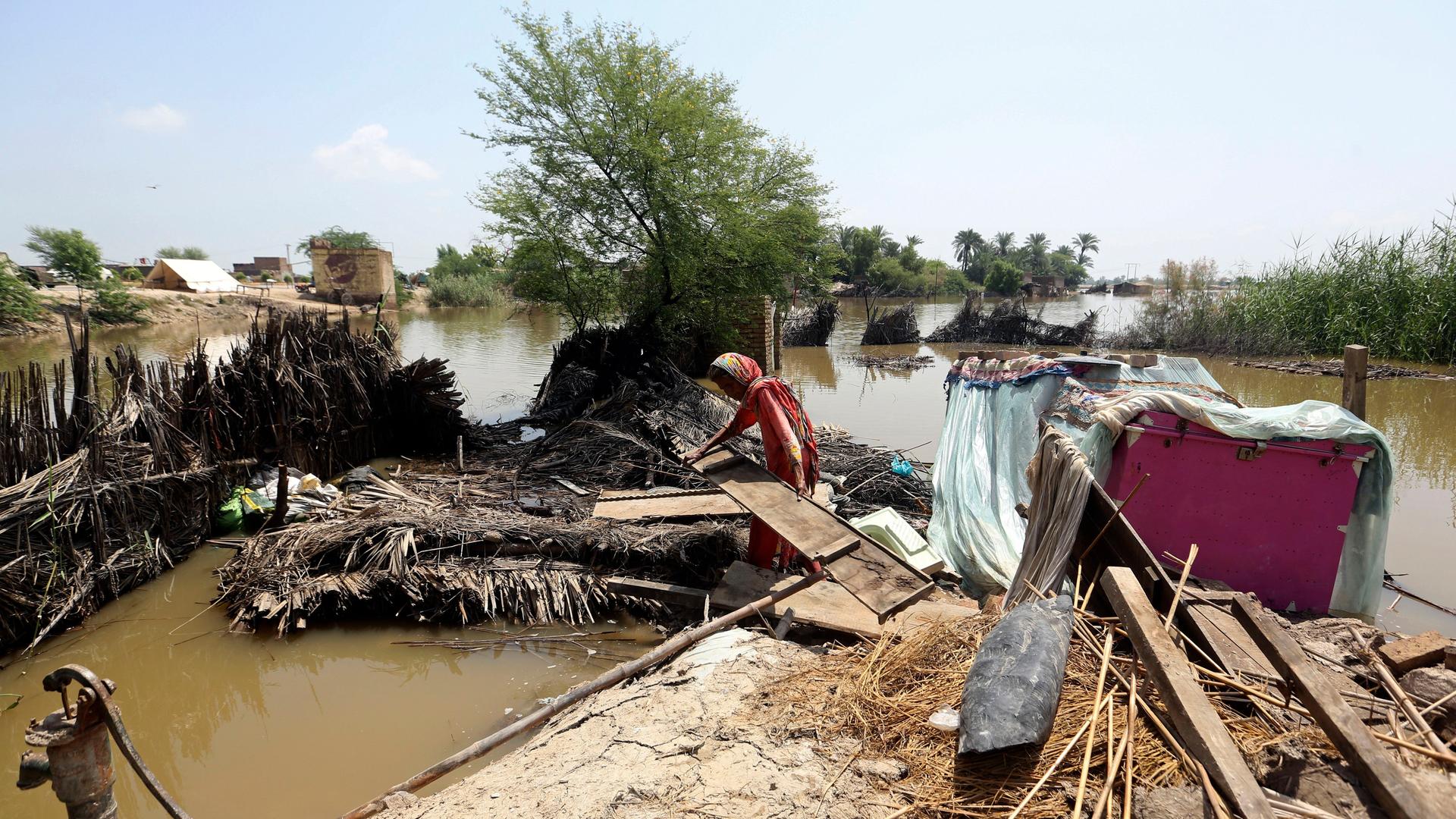 Pakistan Sindh: Eine Frau steht in dem von der Flut zerstörten Haus und räumt ein Brett weg.