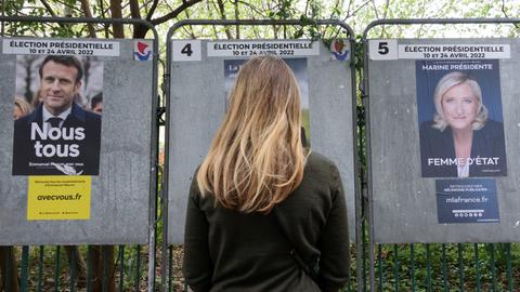 Eine junge Frau steht vor Wahlplakaten von Emmanuel Macron und Marine Le Pen in der Rue de Babylone in Paris, April 2022.