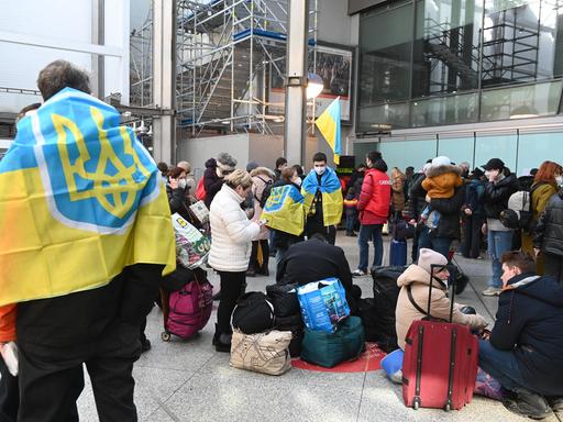 Geflüchtete aus der Ukraine stehen mit Koffern und Flaggen am Münchner Hauptbahnhof (11.3.2022)