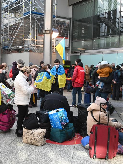 Geflüchtete aus der Ukraine stehen mit Koffern und Flaggen am Münchner Hauptbahnhof (11.3.2022)