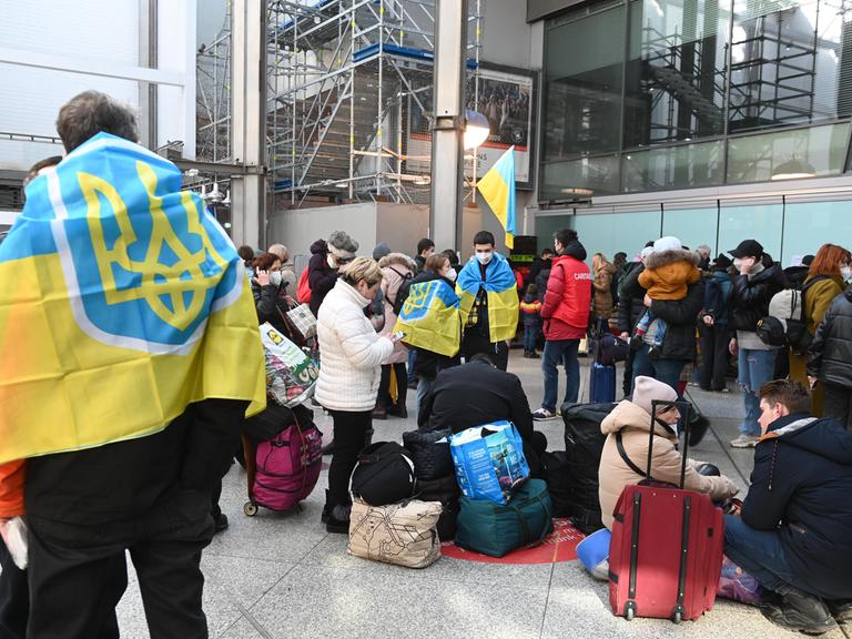 Geflüchtete aus der Ukraine stehen mit Koffern und Flaggen am Münchner Hauptbahnhof (11.3.2022)