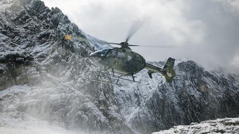 Ein Hubschrauber der Bundeswehr im Flug vor verschneiten Bergen