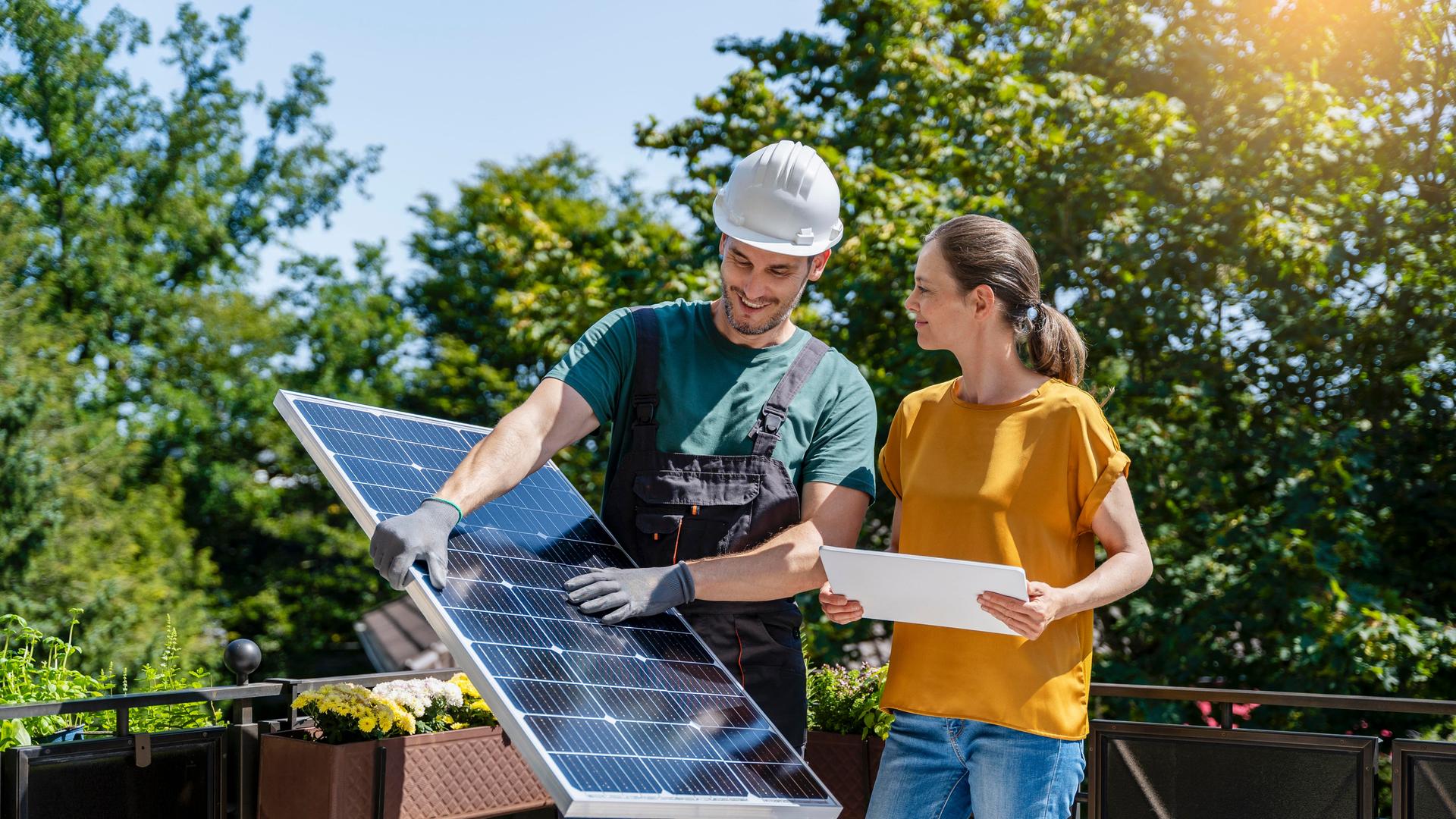 Ingenieur diskutiert mit Frau auf Balkon über Solarpanel.