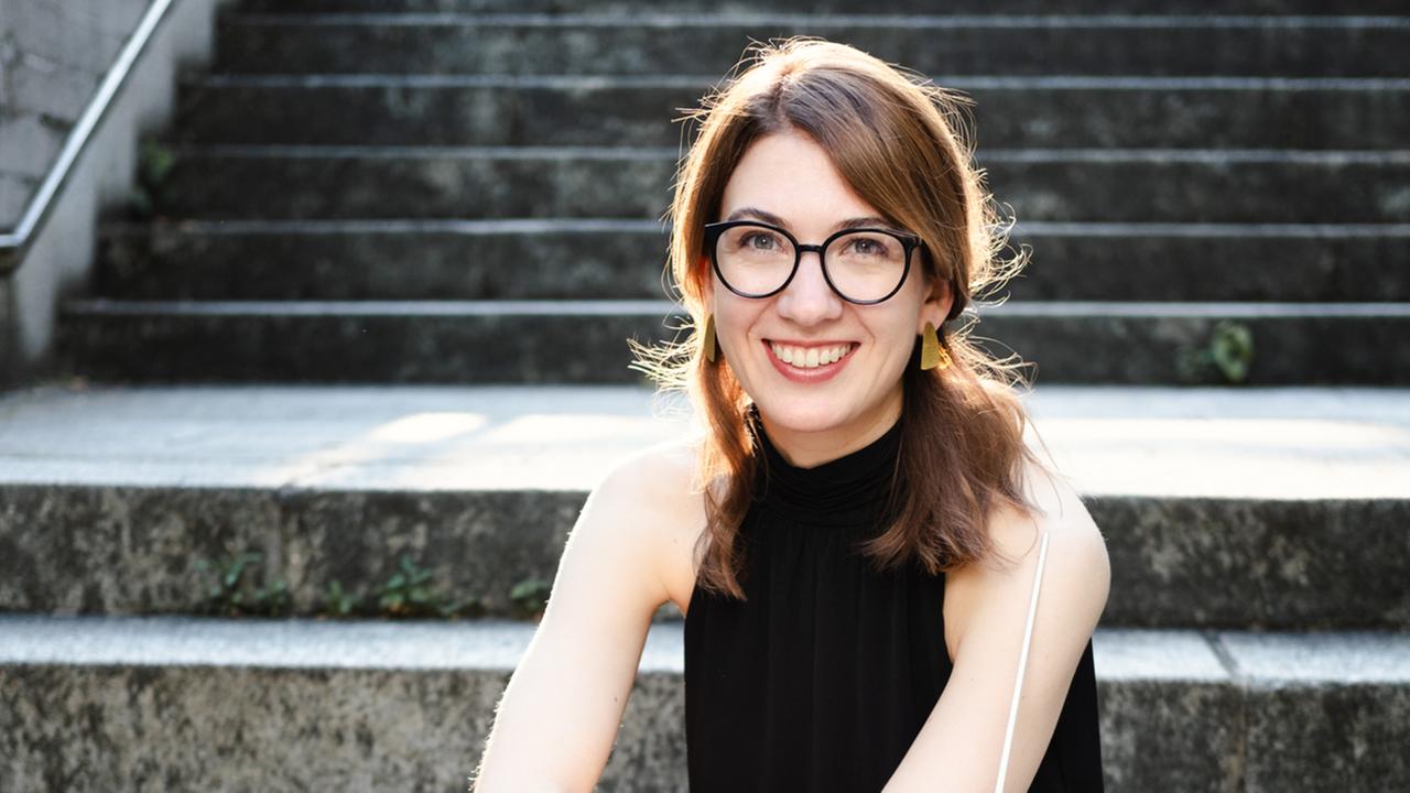 Katharina Morin sitzt auf Steinstufen und lächelt in die Kamera.