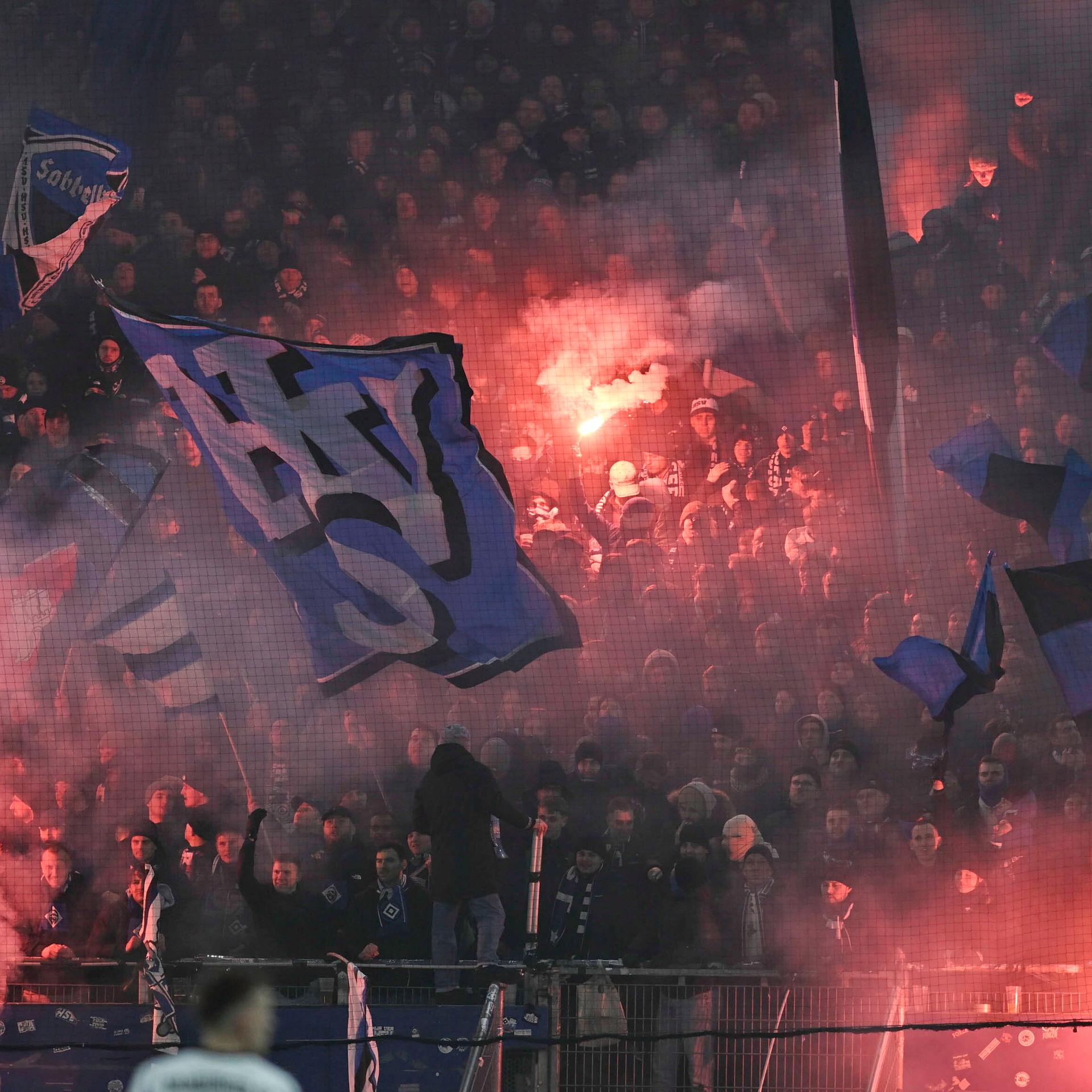 Blick auf den Fanblock des HSV. An mehreren Stellen zünden Fans Pyrotechnik.