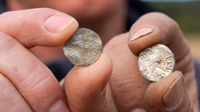 Zwei Hände halten Münzen in die Kamera. Es sind alte Münzen aus der Wikingerzeit. 