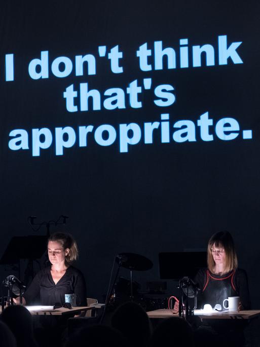 Die Musiker des KNM-campus ensembles sitzen in Reihe auf der Bühne, während über ihnen Sätze an die Wand projiziert werden