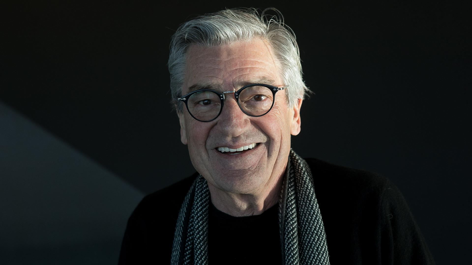 Porträt des lächelnden Dokumentarfilmers Franz Xaver Gernstl, er hat graue Haare und trägt einen Schal über einem schwarzen Pullover