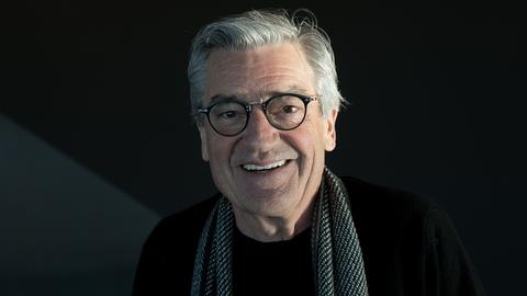 Porträt des lächelnden Dokumentarfilmers Franz Xaver Gernstl, er hat graue Haare und trägt einen Schal über einem schwarzen Pullover