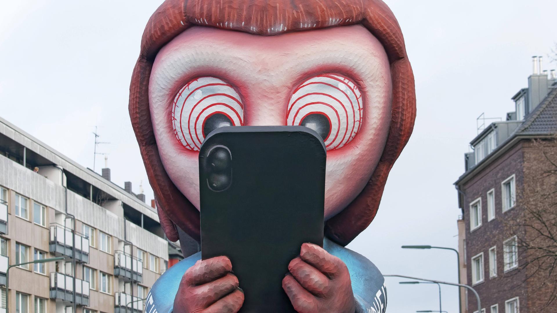 Kind starrt mit großen Augen aufs Handy (Mottowagen von Wagenbauer Jacques Tilly, Düsseldorfer Rosenmontagszug)