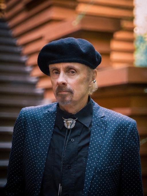 Der Autor T.C. Boyle schaut ernst in die Kamera. Er hat einen kurzen, grau melierten Bart und trägt eine schwarze Baskenmütze, ein schwarzes Hemd und darüber ein blaues Jackett mit weißen Punkten.